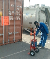 A pest control technician standing outside a cargo container operating fumigation equipment.